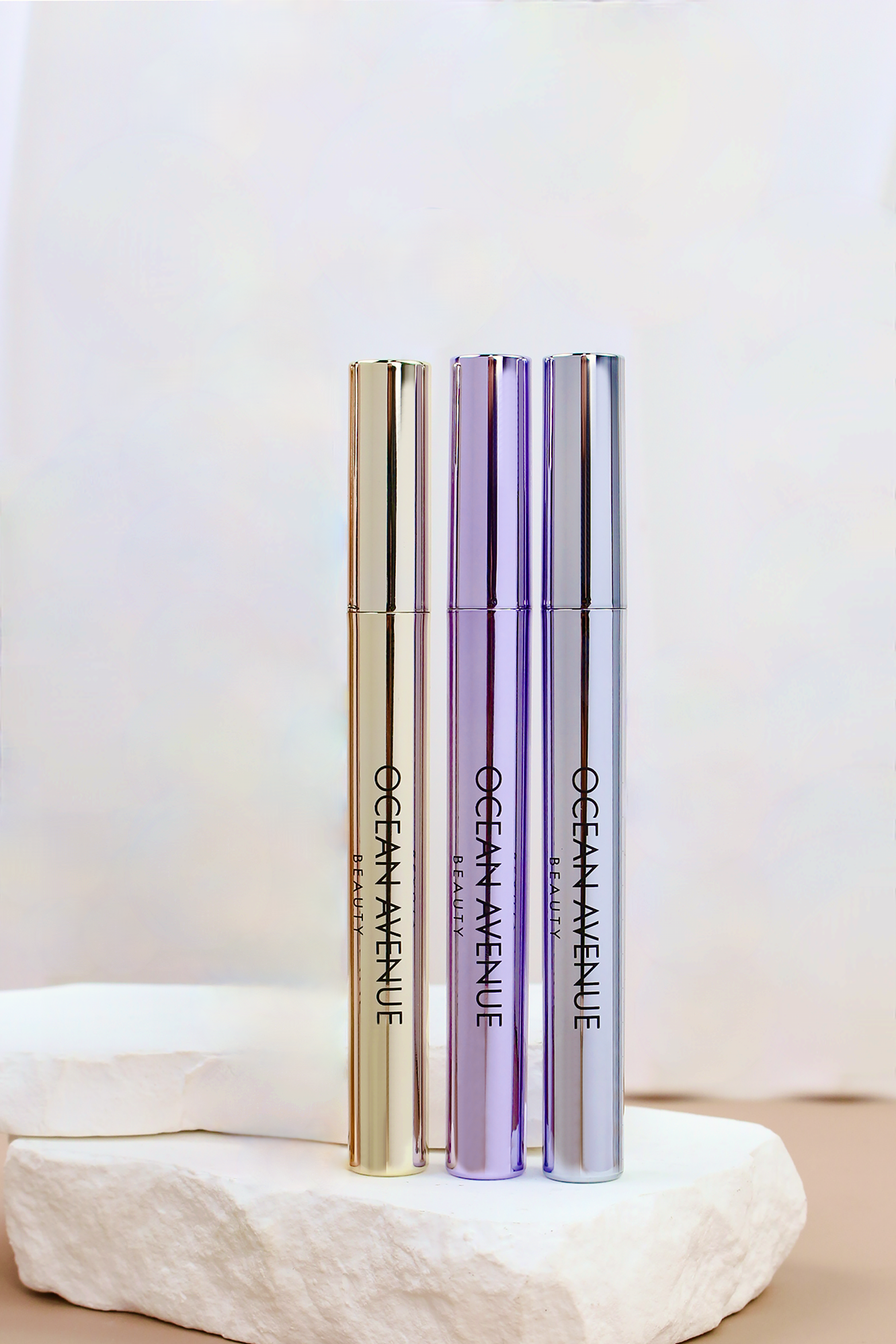 Ocean Avenue Beauty peel-off lip stain trio—three metallic tubes on a stone pedestal.