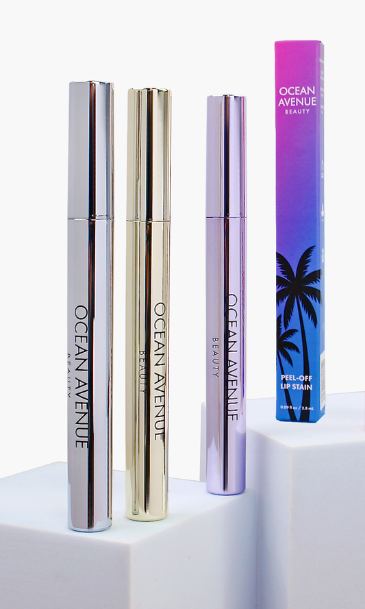 Ocean Avenue Beauty peel-off lip stain trio—silver, gold and lavender tubes with retail box on white pedestals.